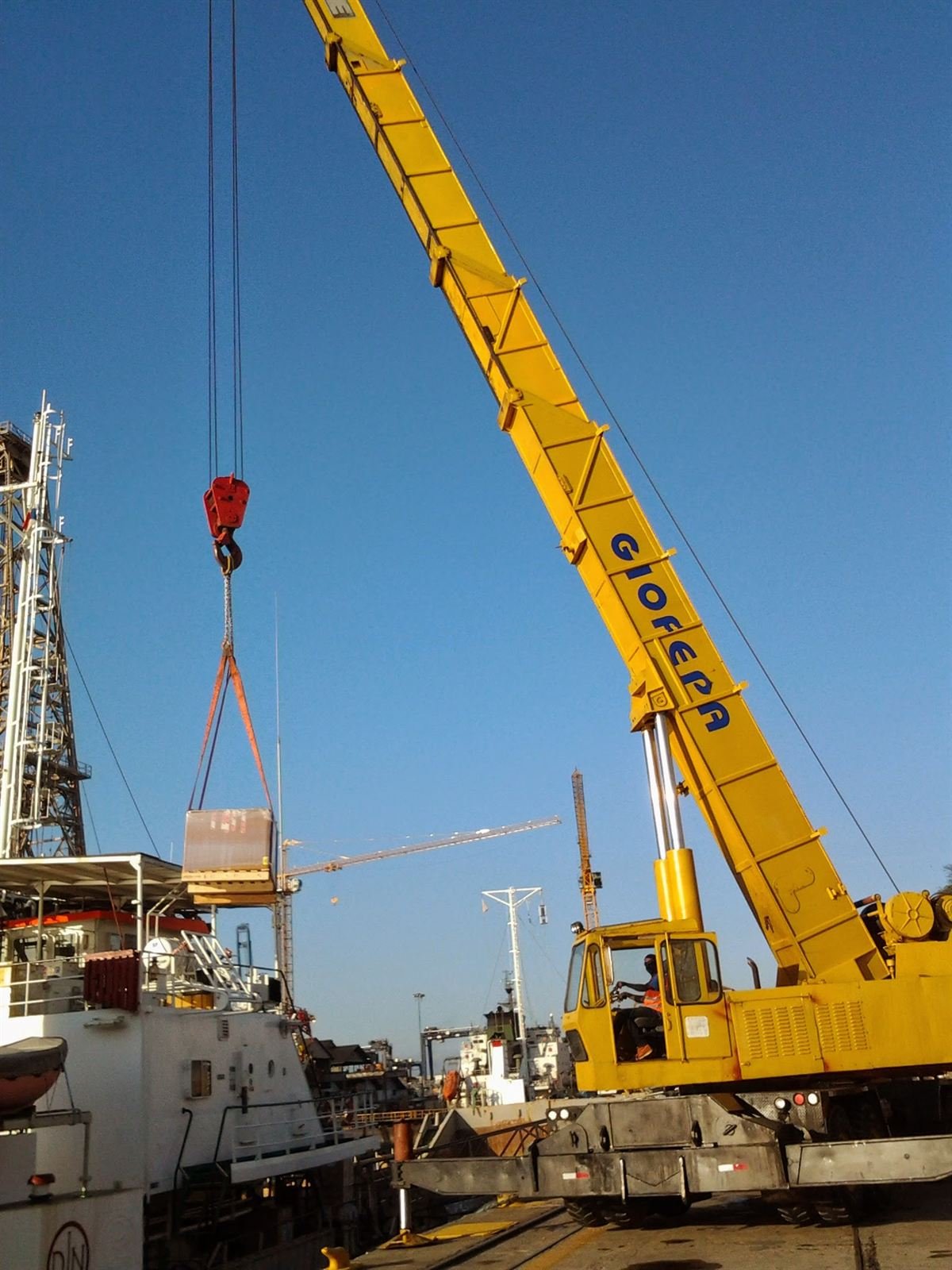 Grúa móvil izando carga hacia buque en muelle